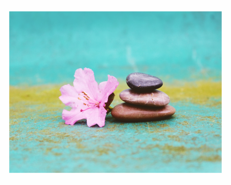 Moment zen avec trois jolis galets en équilibre sur un fond bleu - une fleur d’hibiscus rend cet ensemble très joli