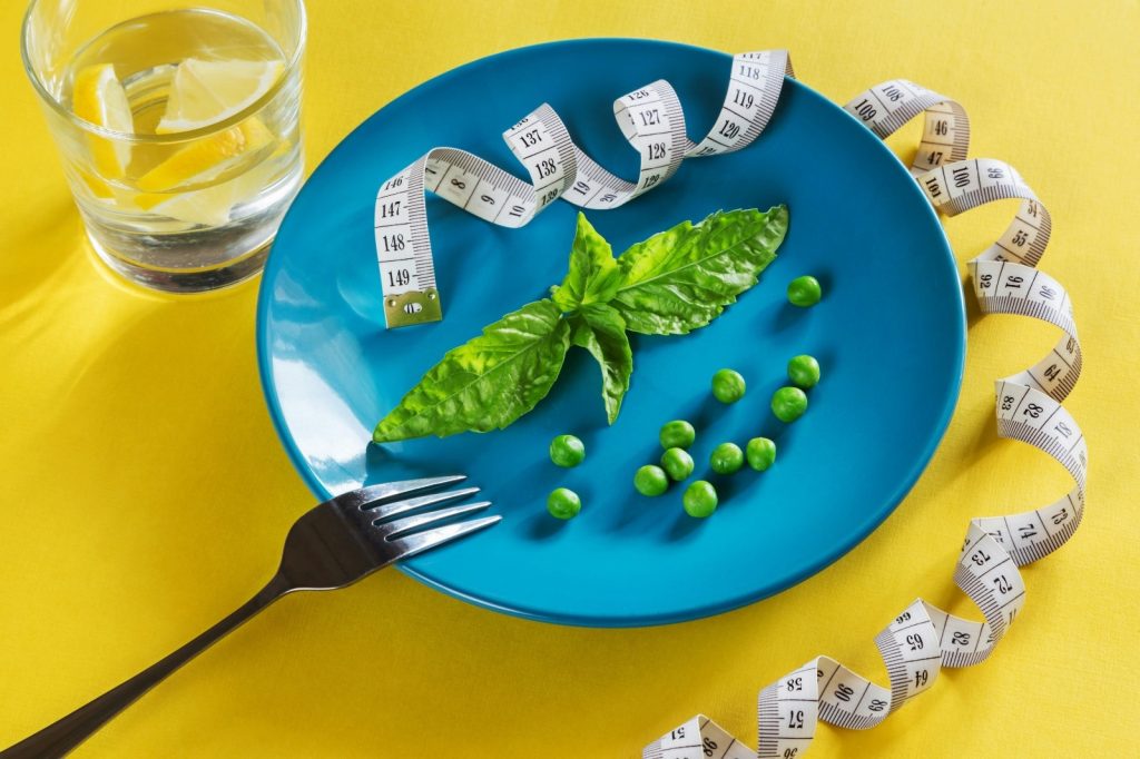 Perdre du poids avec la Naturopathie - Assiette bleu avec des petits pois et un centimètre sur une table jaune