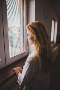 Jeune femme pensive regardant par la fenêtre, évoquant la surcharge mentale chez une personne sensible