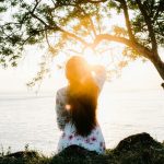 une femme assise face à la mer et au soleil